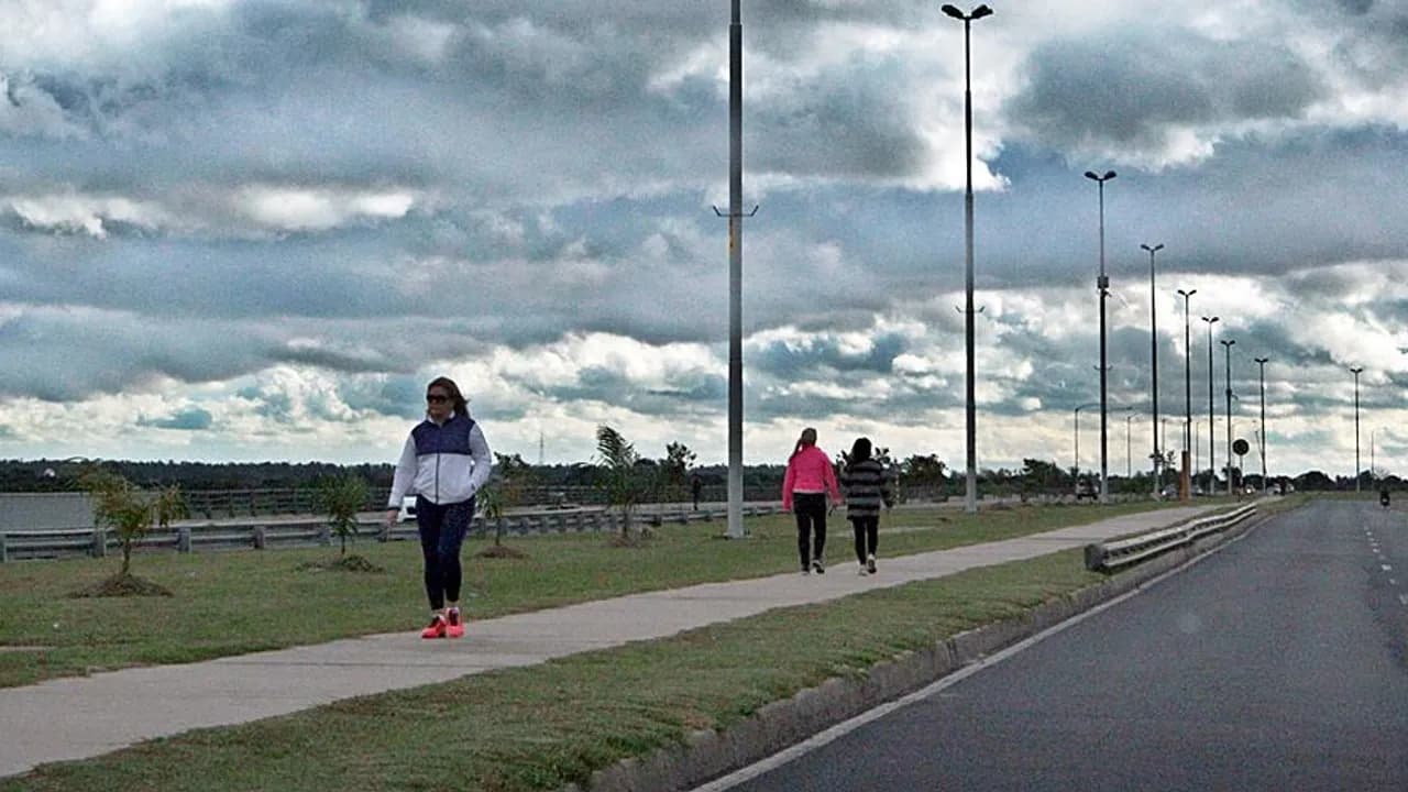 Personas caminando por una caminera al aire libre bajo un cielo nublado al costado de la avenida.