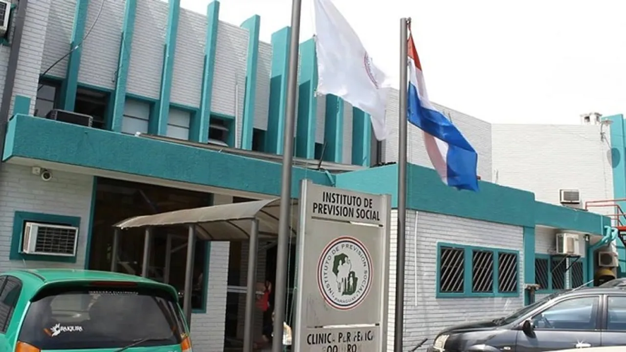 Fachada del edificio de la sede de salud con el cartel indicador de la institución y la bandera nacional.