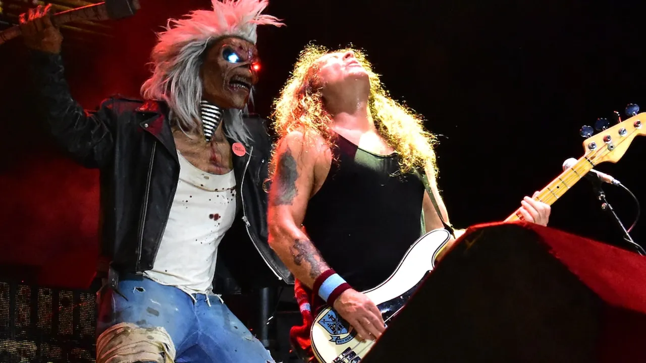 Steve Harris toca el bajo en un escenario iluminado junto a Eddie, la mascota de la banda con ojos brillantes.