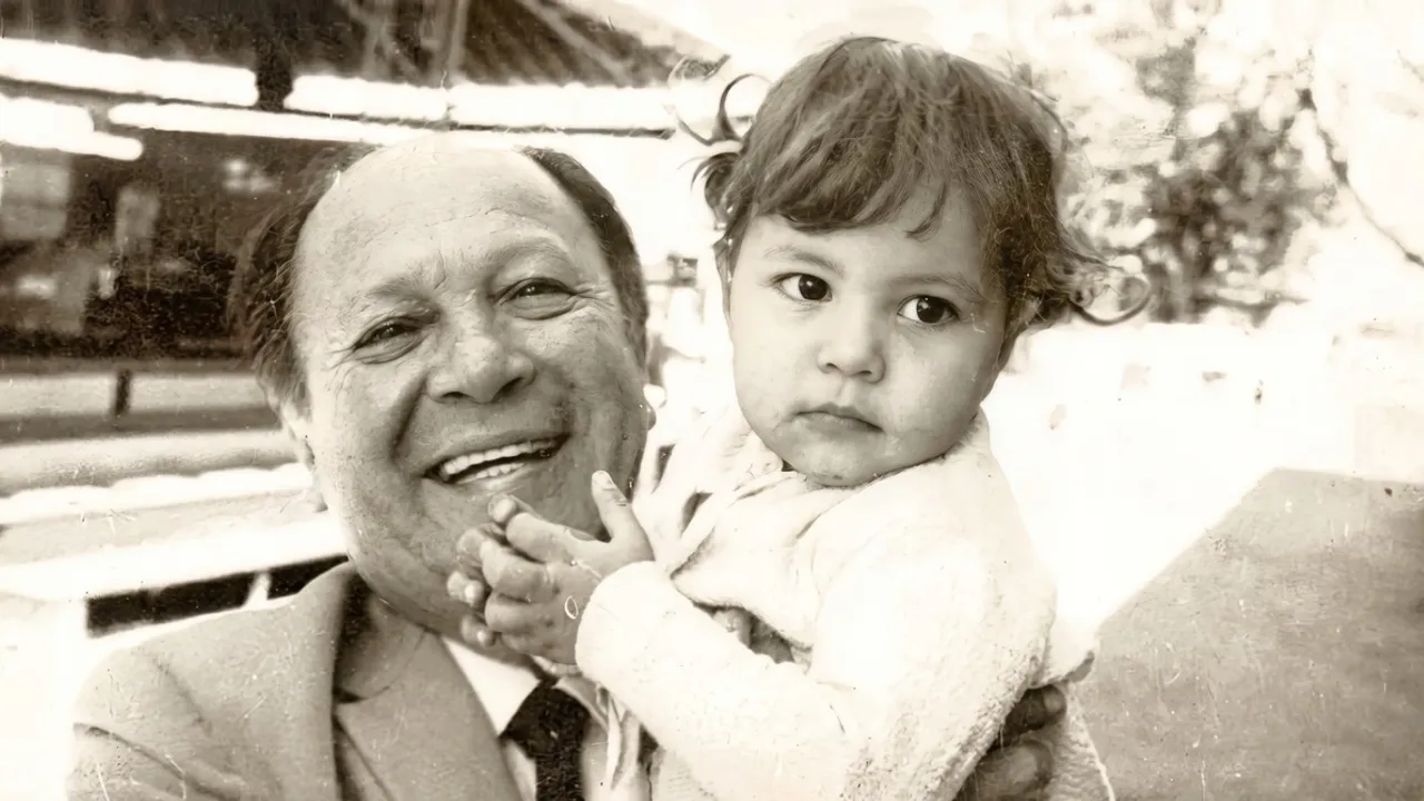 Retrato en blanco y negro del compositor José Asunción Flores sonriendo mientras sostiene a una niña pequeña.