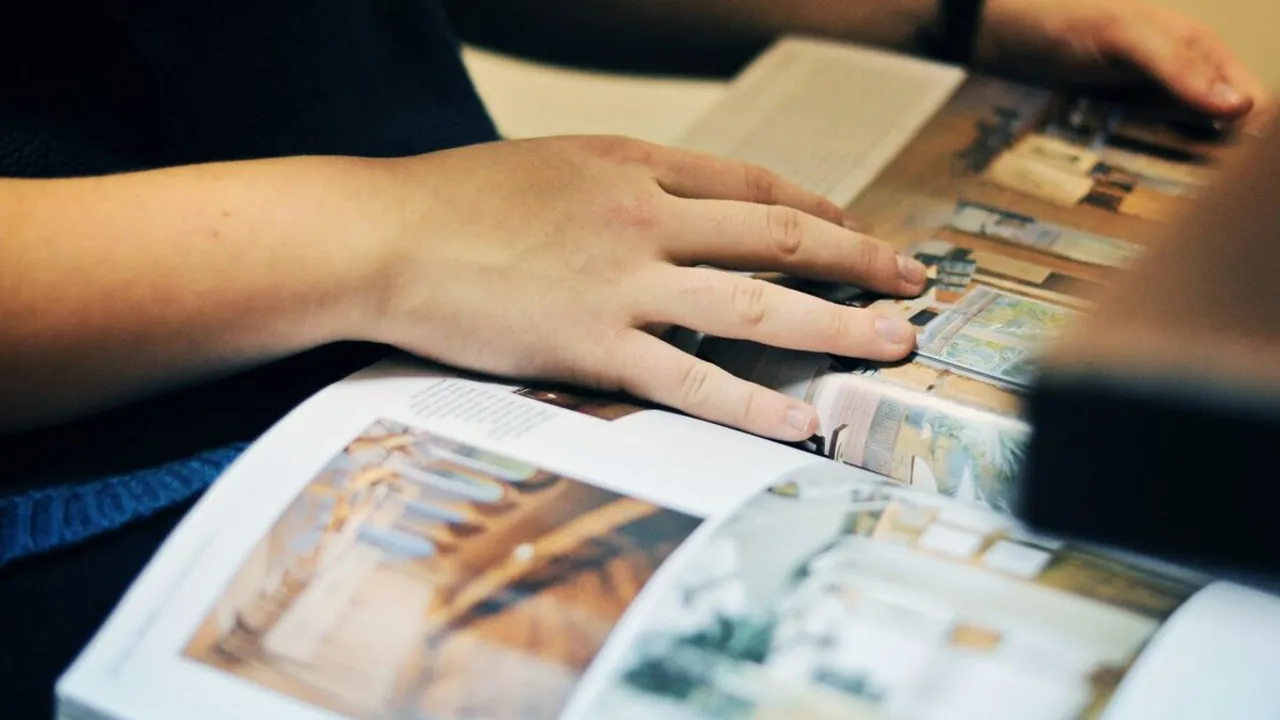 Manos de una persona hojeando una revista abierta con fotografías a color de interiores y arquitectura.