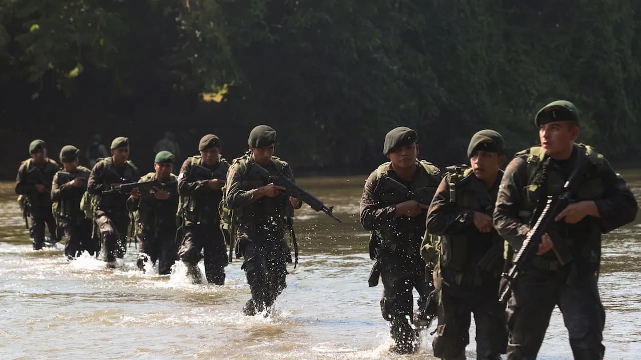 Soldados con uniforme de camuflaje y fusiles avanzan en fila cruzando las aguas de un río durante una operación militar.