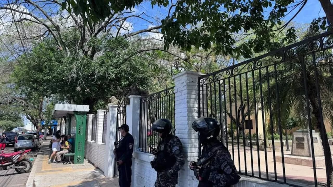 Agentes policiales con cascos y chalecos tácticos custodian la vereda frente a la reja de un colegio en Asunción.
