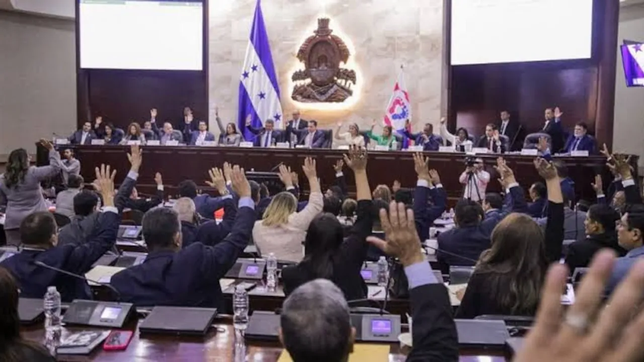 Diputados sentados en el hemiciclo legislativo levantan la mano para votar durante una sesión plenaria oficial.