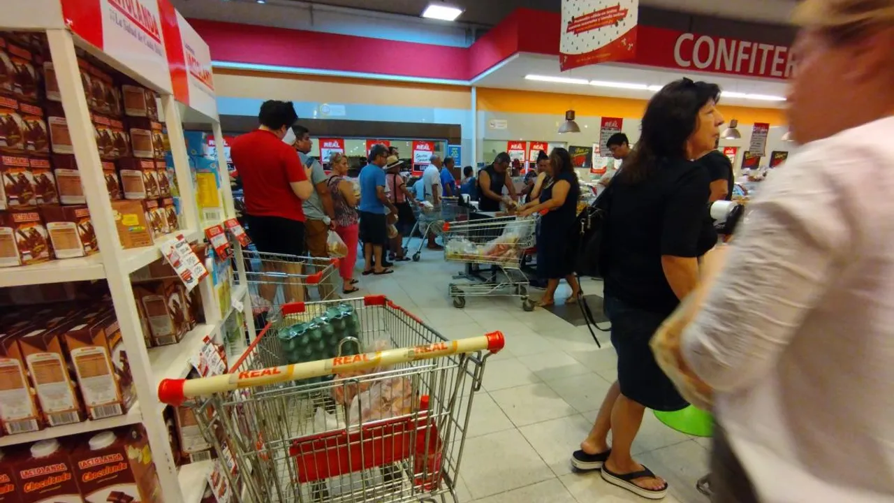 Personas con carritos de supermercado formando fila frente a góndolas y cajas de cobro.
