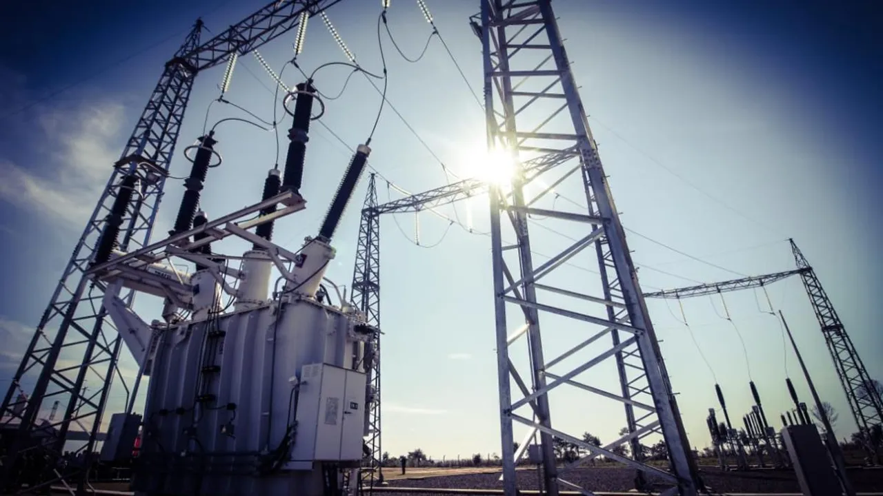 Transformador y torres metálicas de alta tensión en una subestación eléctrica bajo la luz directa del sol.