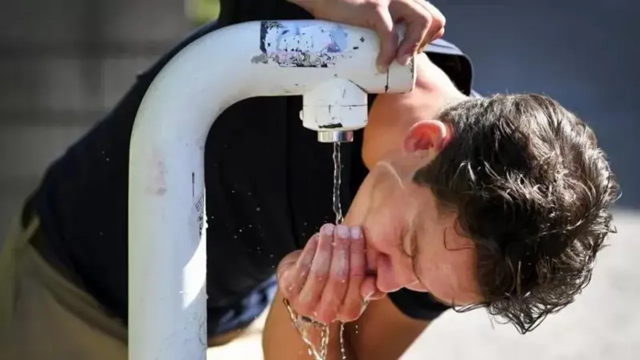 Un joven inclinado bebe agua fresca directamente de una fuente pública al aire libre.