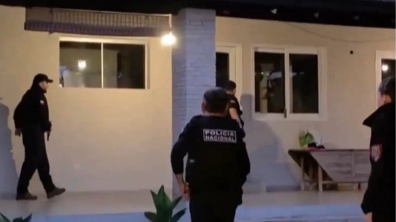 Agentes de la Policía Nacional ingresan al patio iluminado de una vivienda durante un allanamiento nocturno.