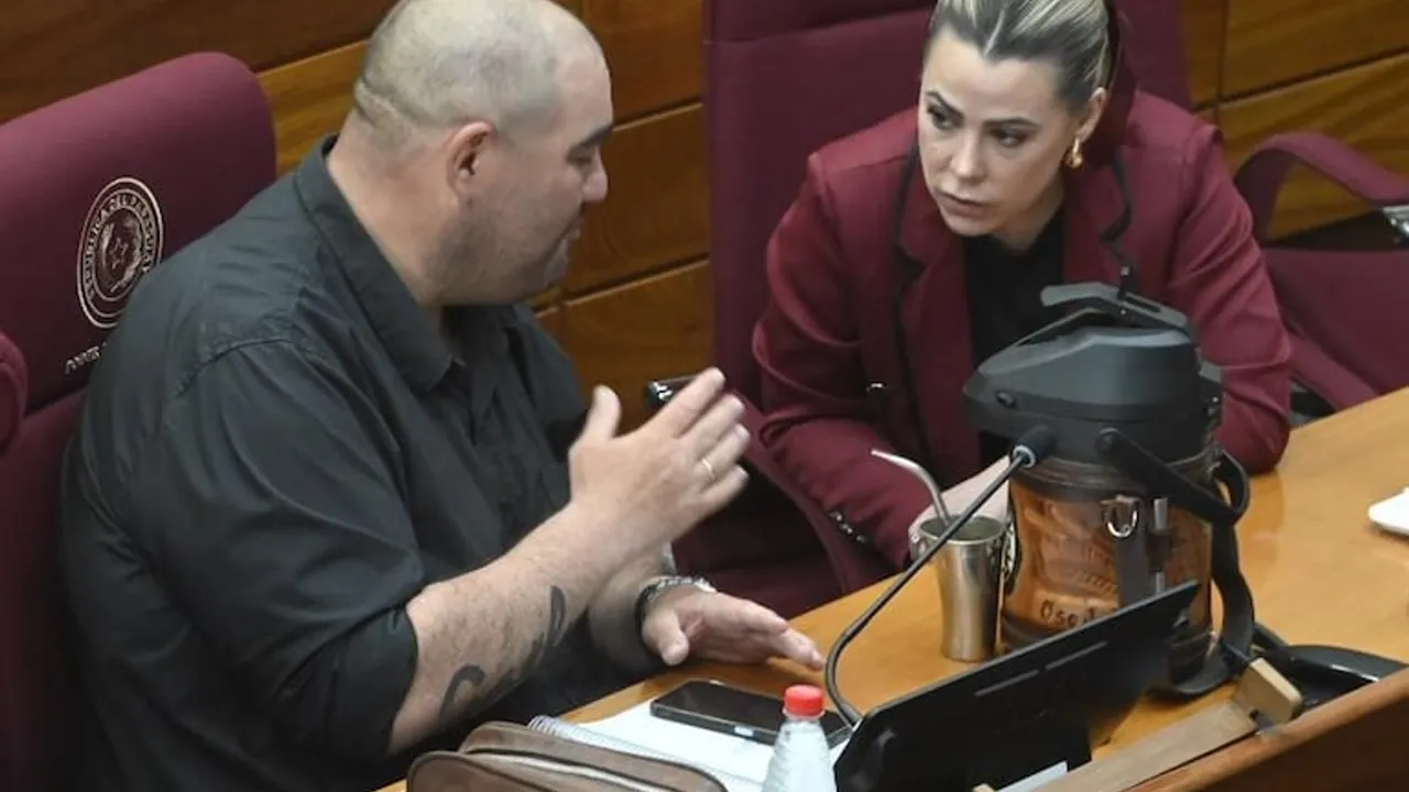 Dos legisladores conversan en sus bancas durante una sesión parlamentaria en el Congreso Nacional.