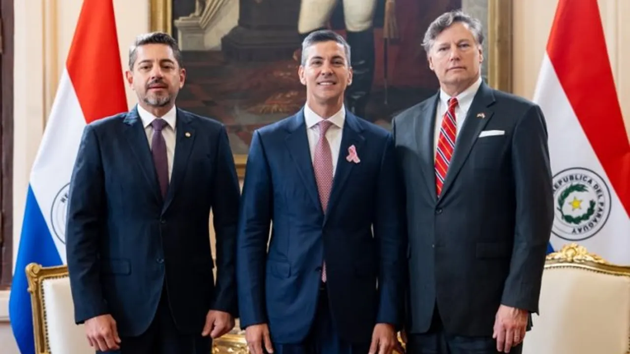 Pedro Alliana, Santiago Peña y Christopher Landau posan de pie en un salón oficial junto a banderas patrias.