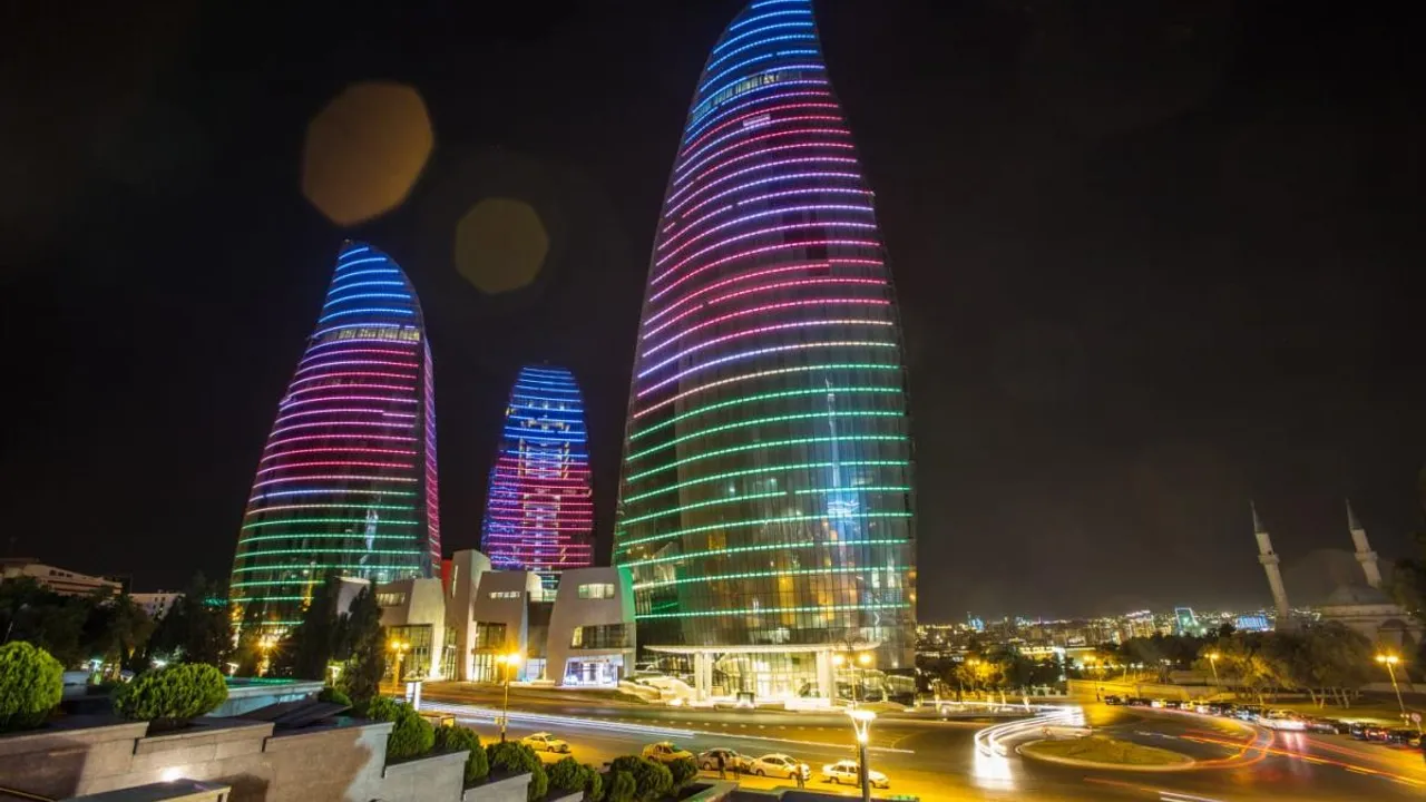 Tres rascacielos iluminados con luces de colores durante la noche en una moderna avenida urbana de Bakú.
