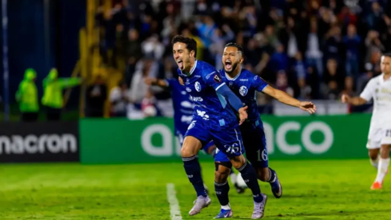 Dos futbolistas con uniforme azul celebran con euforia en el campo de juego durante un partido nocturno.