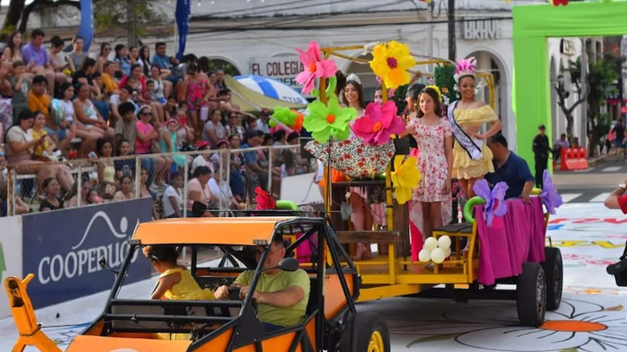 Carro alegórico decorado con flores gigantes y jóvenes saludando durante un desfile callejero concurrido.