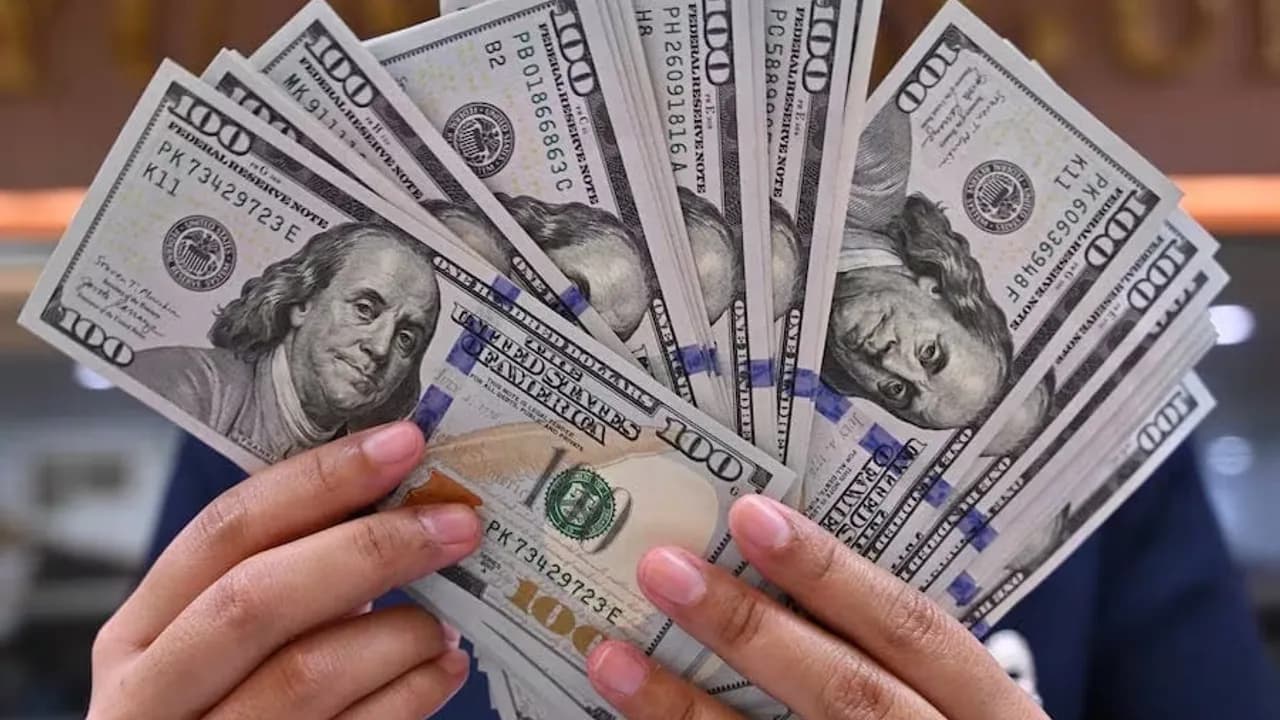 Persona sosteniendo un abanico abierto de billetes de cien dólares estadounidenses con ambas manos.