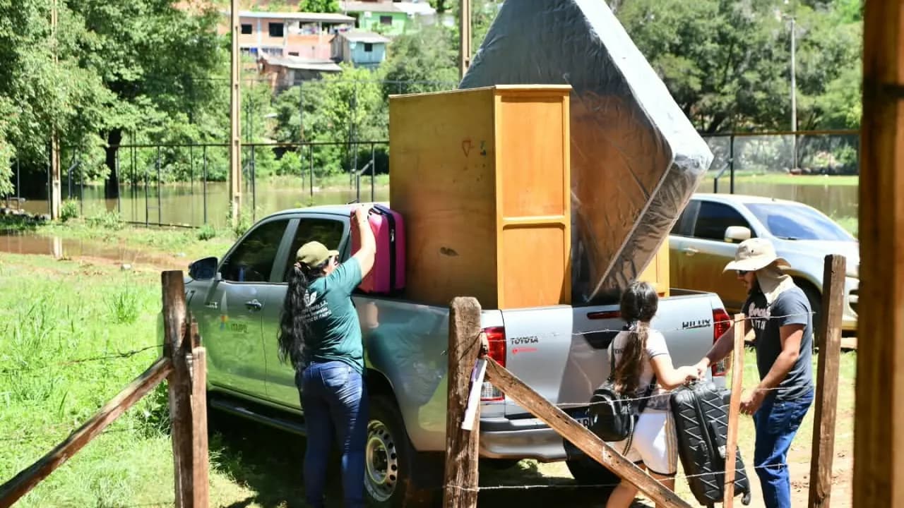 Personas cargan muebles, un colchón y maletas en la carrocería de una camioneta en una zona ribereña.