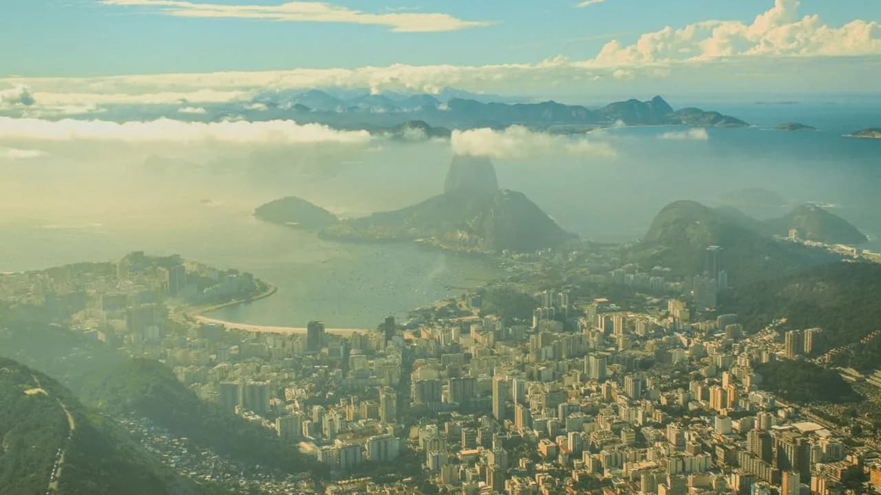 Vista aérea panorámica de Río de Janeiro con rascacielos urbanos, colinas boscosas y la costa bajo nubes bajas.
