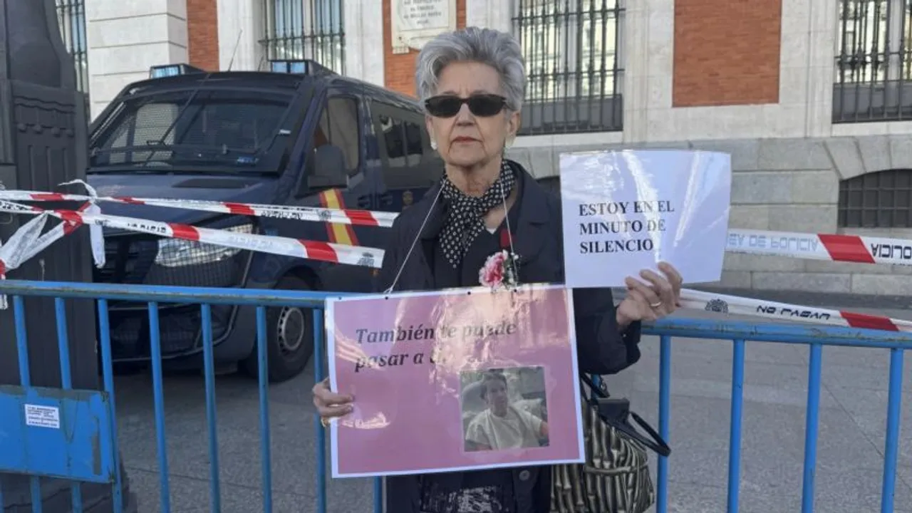 Mujer con gafas oscuras sostiene carteles de protesta frente a un vallado policial en una calle de Madrid.