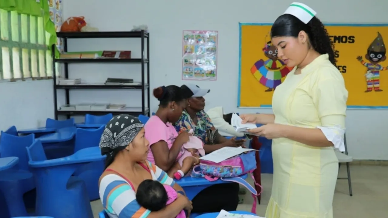 Una enfermera de uniforme claro atiende a madres con sus bebés sentadas en un centro de salud comunitario.