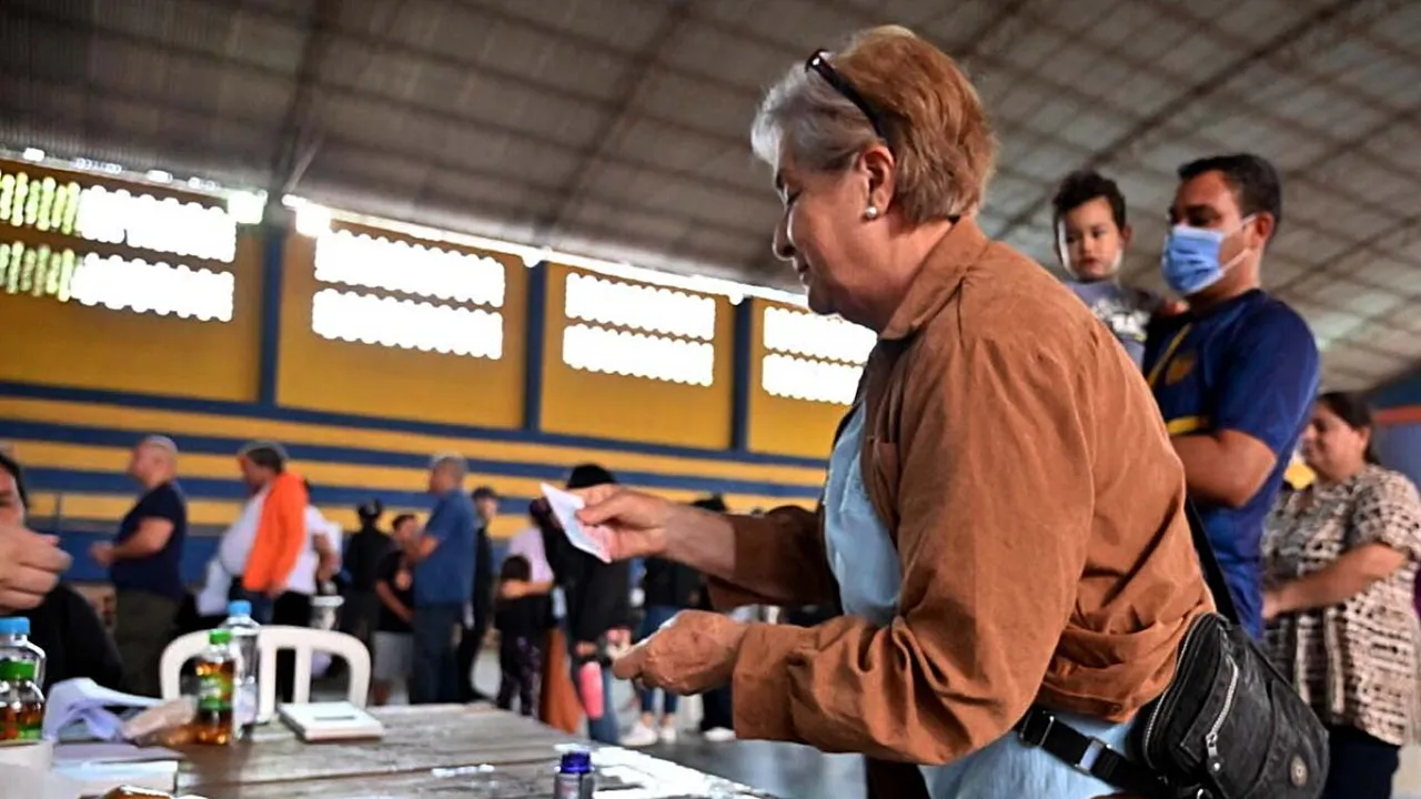 Mujer de perfil entregando su papeleta de votación a las autoridades de mesa en un local electoral comunitario