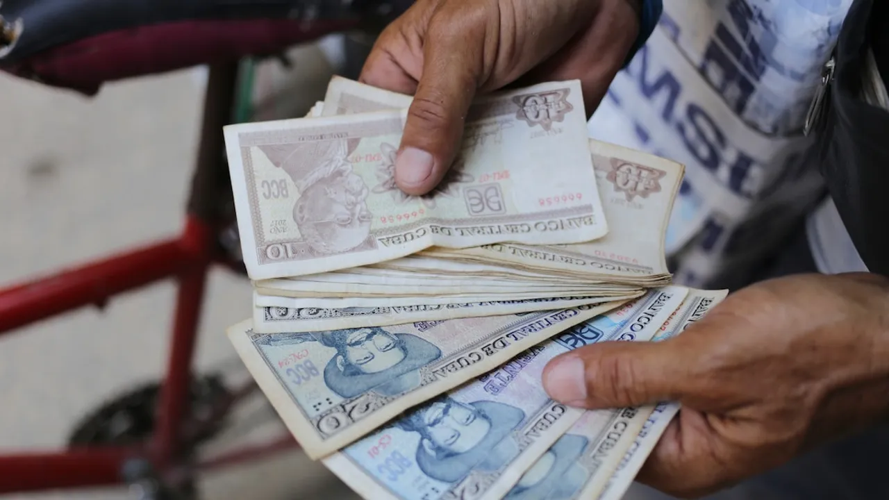 Unas manos sostienen varios billetes de pesos cubanos de diez y veinte junto al manillar de una bicicleta.