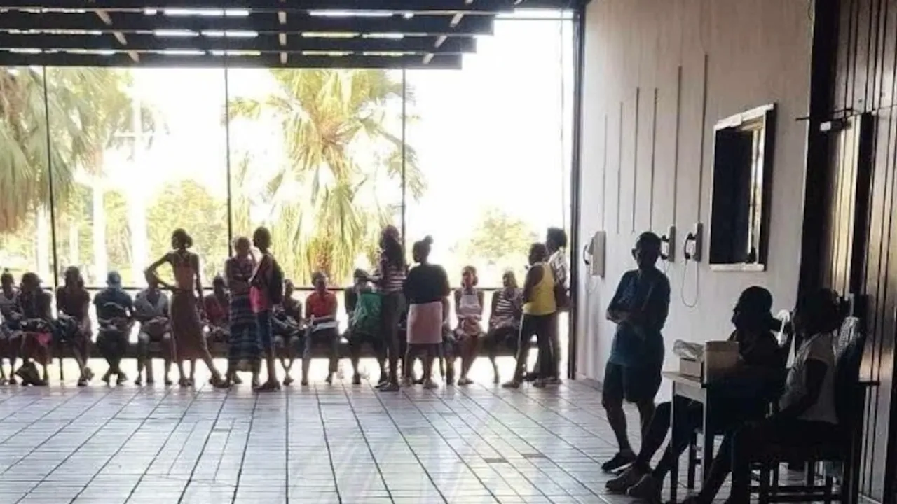 Personas hacen fila y esperan sentadas en una galería techada para retirar dinero en una oficina bancaria.
