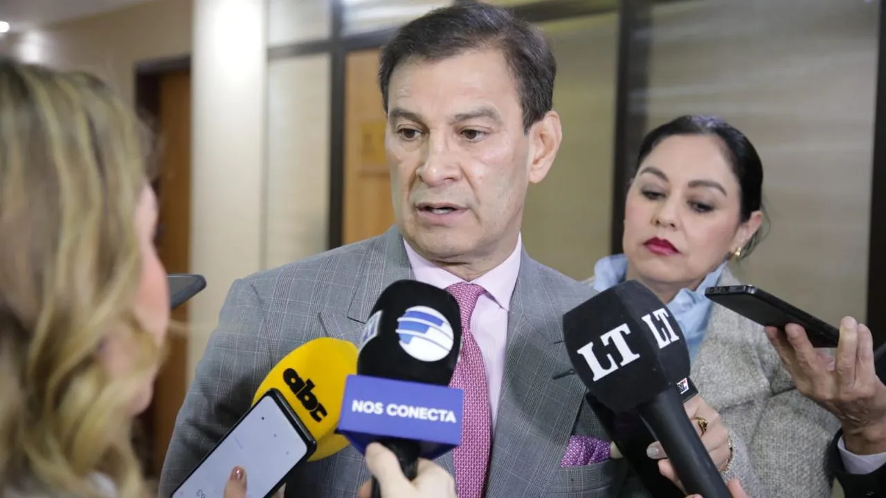 Silvio Beto Ovelar conversa en un pasillo frente a micrófonos y teléfonos de periodistas de prensa.