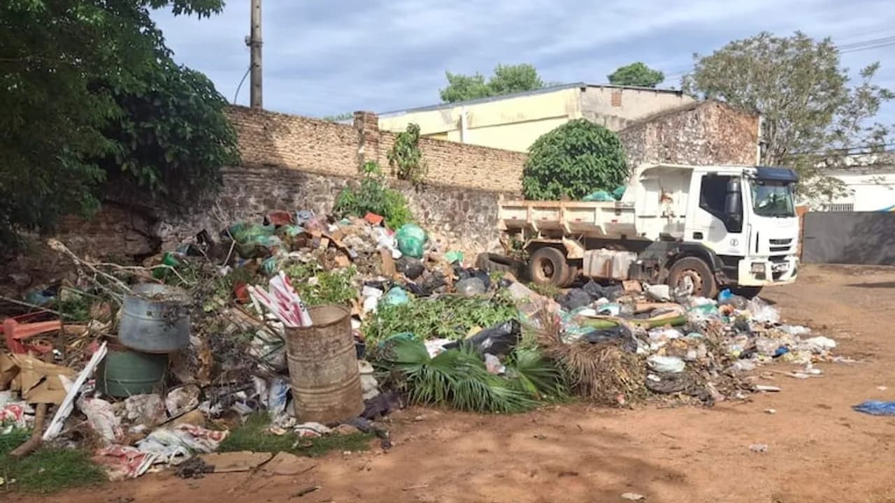 Camión volquete estacionado junto a un gran montículo de basura en un patio de tierra.