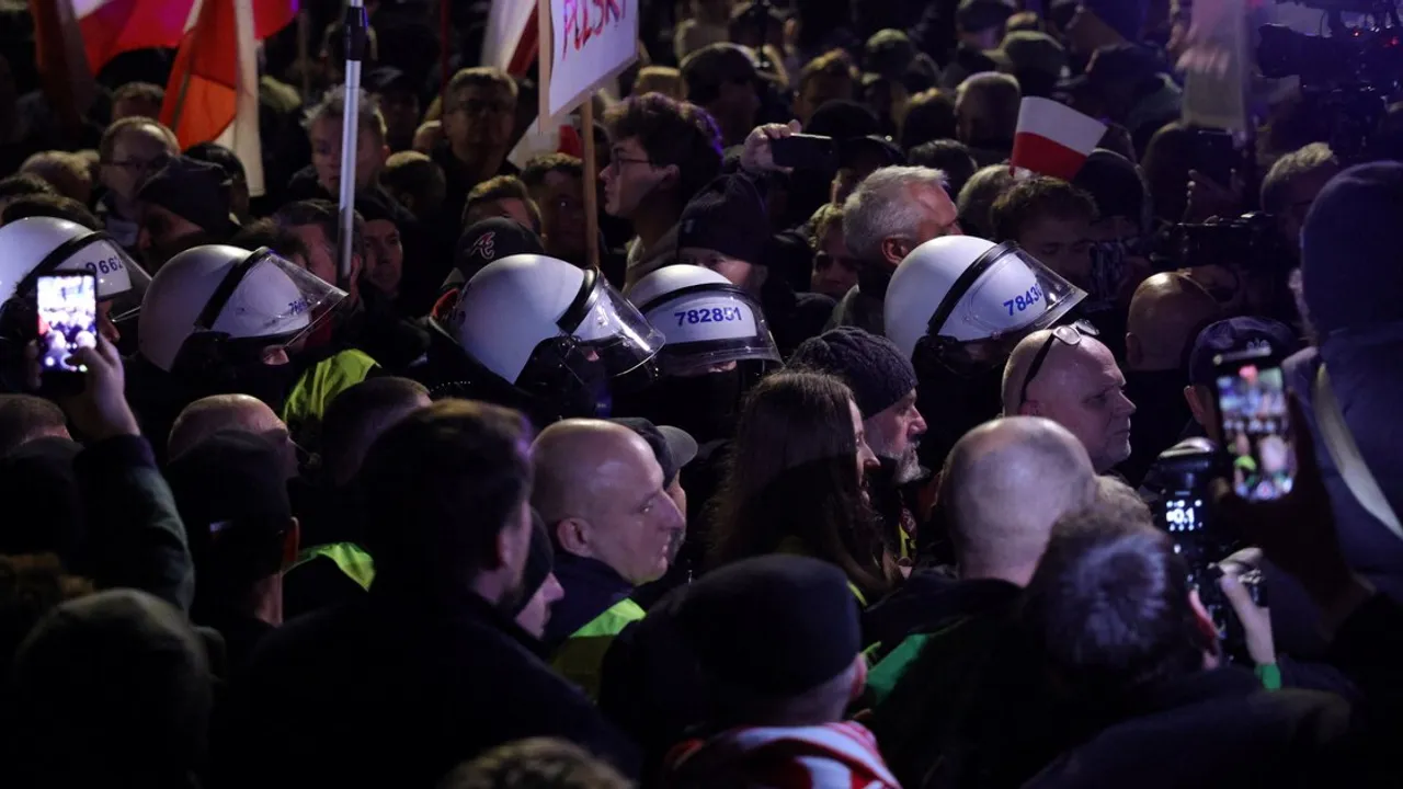 Agentes policiales con cascos y escudos contienen a una multitud de manifestantes con banderas polacas de noche.