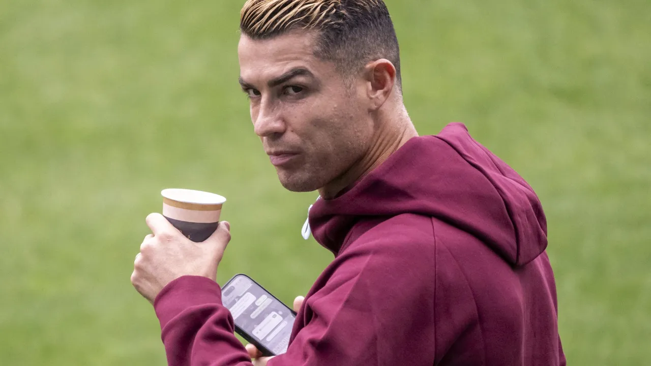 Cristiano Ronaldo sostiene un vaso descartable y un teléfono mientras mira de perfil durante una práctica.