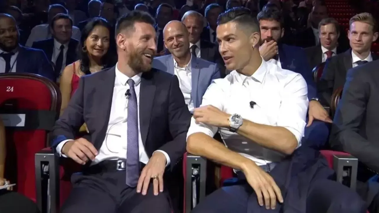 Lionel Messi y Cristiano Ronaldo sonríen y conversan sentados con trajes de gala durante una premiación deportiva