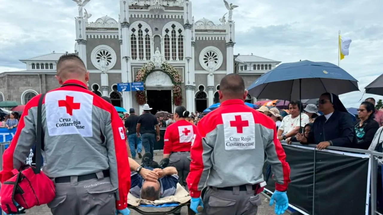 Socorristas con uniformes de la Cruz Roja trasladan a un hombre en camilla frente a una multitud y una iglesia.