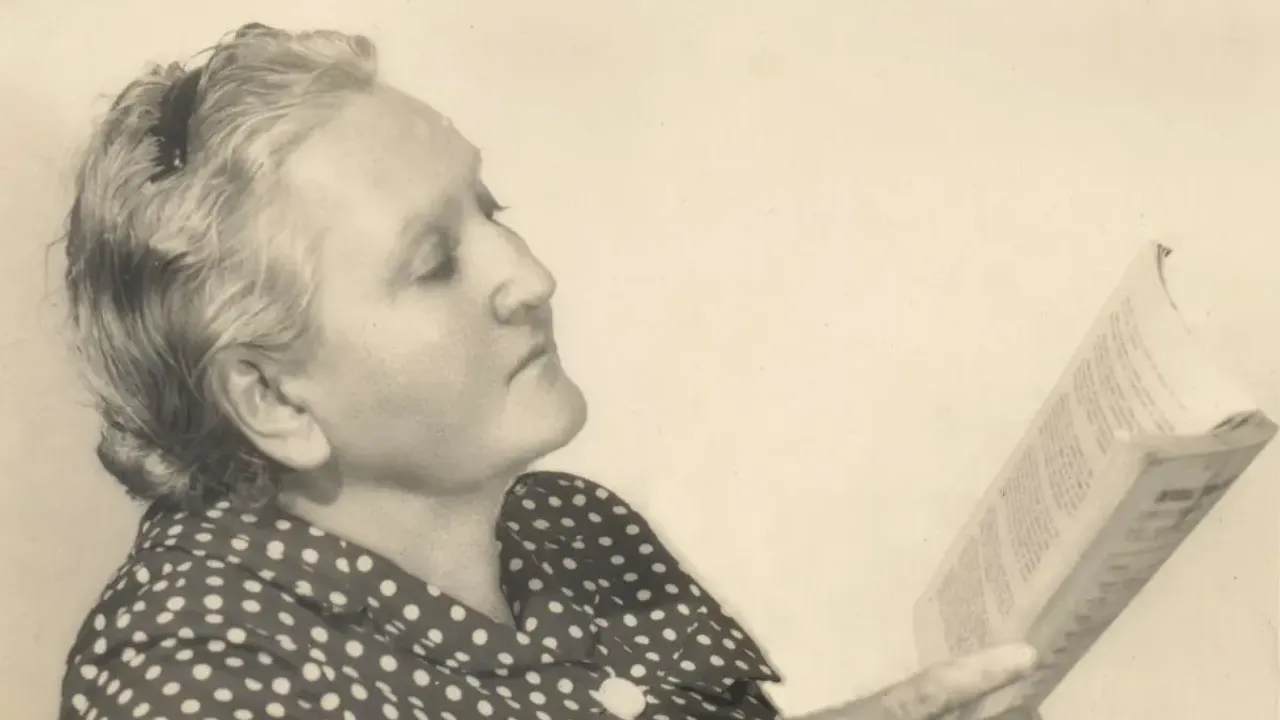 Retrato en blanco y negro de perfil de una mujer con blusa a lunares sosteniendo y leyendo un libro abierto.