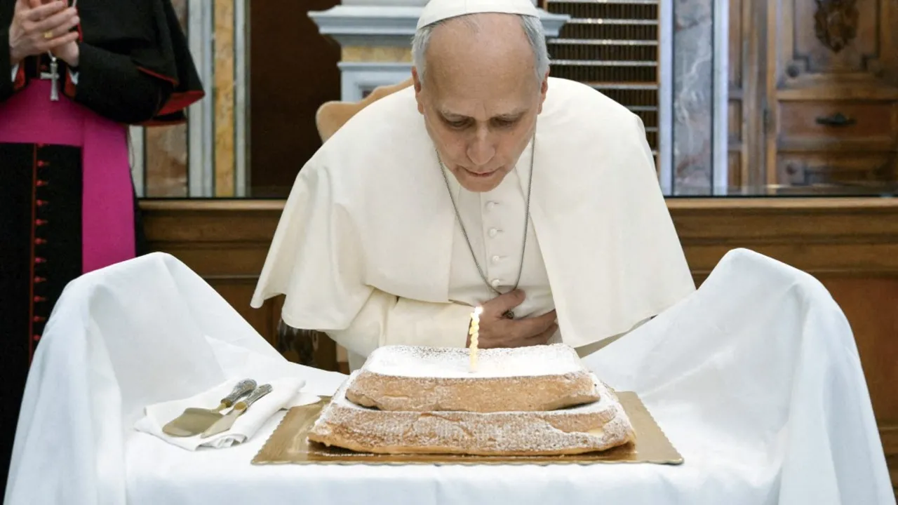 El pontífice con vestimenta blanca inclinado sobre una torta con azúcar impalpable apagando una vela.