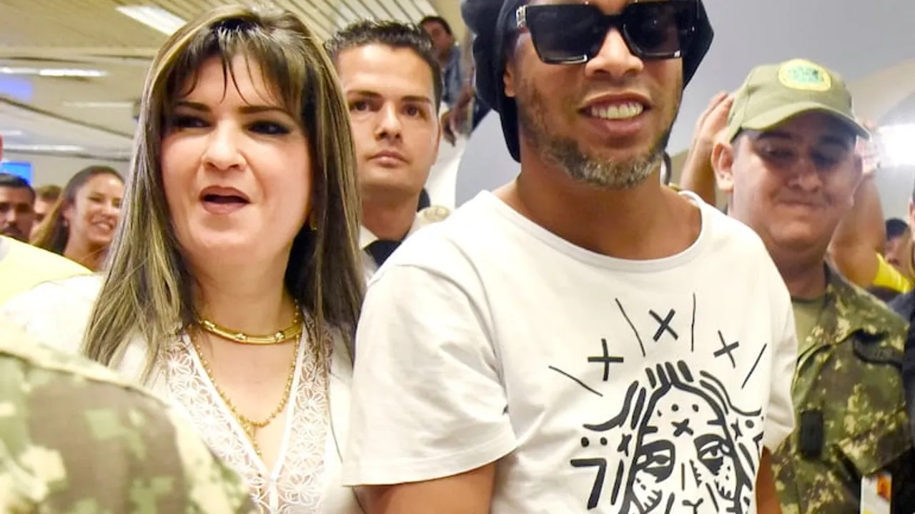 Ronaldinho sonríe junto a Dalia López en medio de una multitud y agentes de seguridad en un aeropuerto.