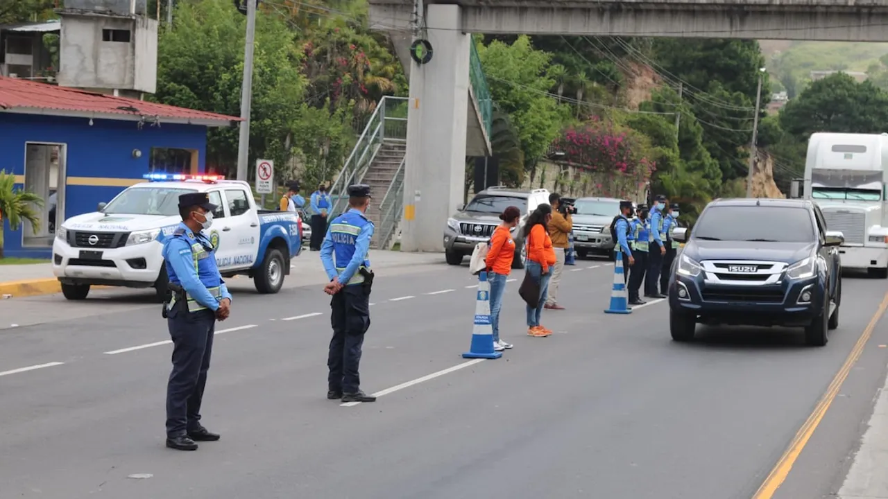 Agentes policiales con mascarillas realizan un control de tránsito en una autopista con conos viales y camionetas.