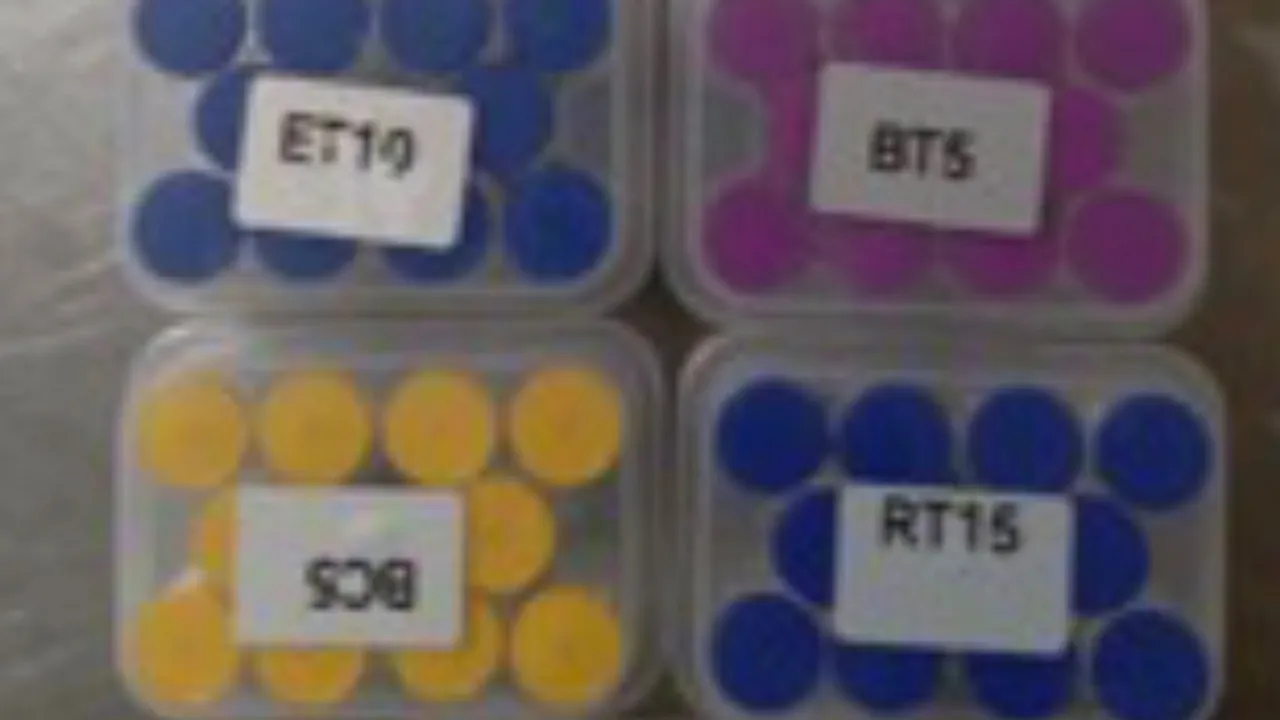 Cuatro cajas de plastico transparente con pequenos frascos de tapas azules, amarillas y violetas con codigos.