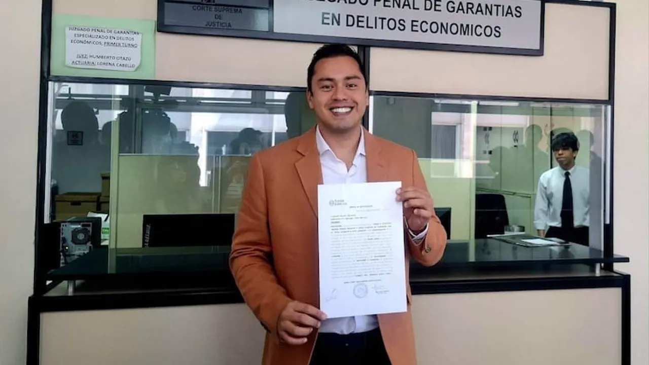 Miguel Prieto sonríe sosteniendo una notificación judicial frente a la ventanilla del juzgado en delitos económicos.