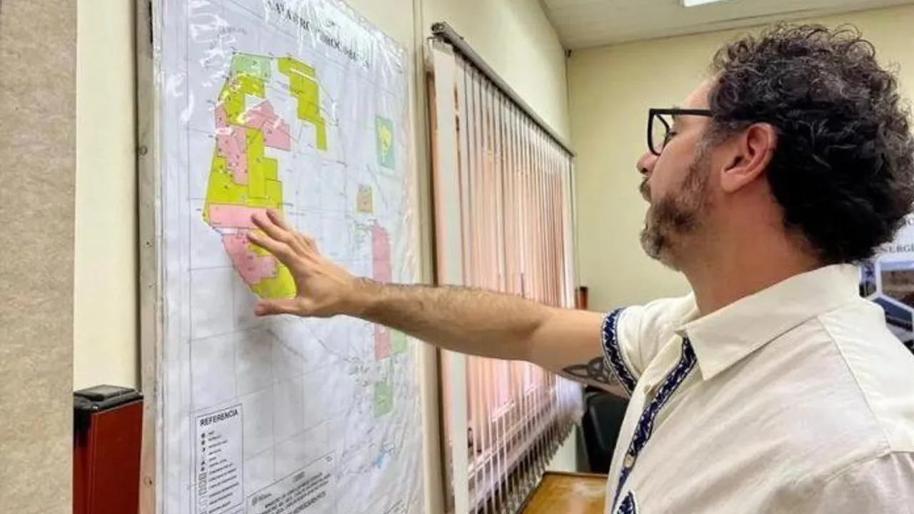 Mauricio Bejarano de perfil señalando con la mano un mapa cartográfico colgado en una pared de oficina