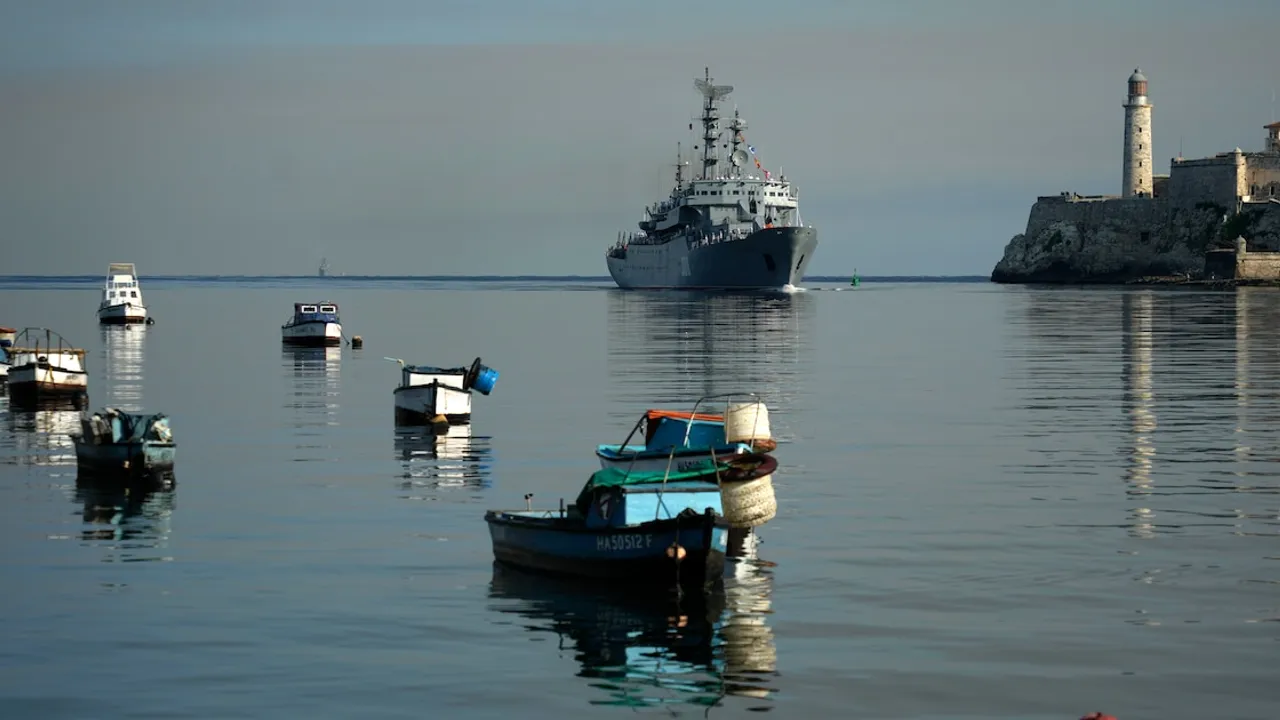 Botes pesqueros en una bahía con un gran buque militar navegando de fondo cerca de una torre de faro costero.