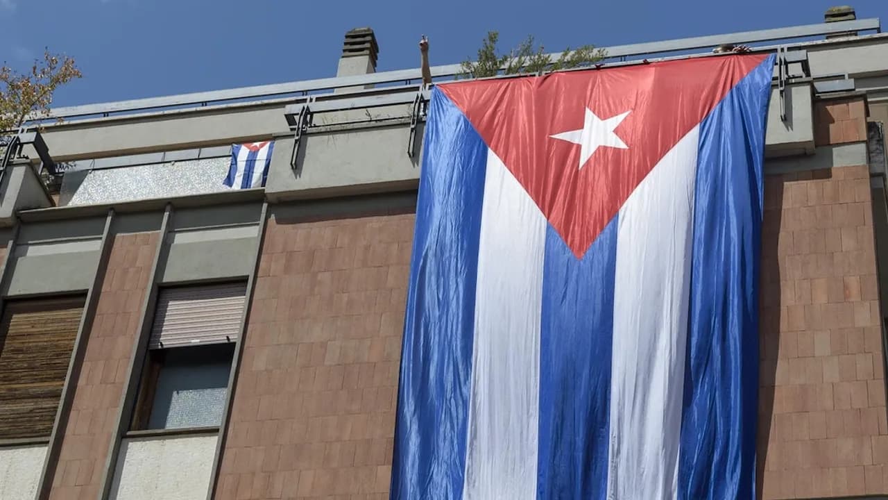 Bandera cubana de gran tamaño colgada de la terraza de un edificio bajo el cielo despejado durante el día.