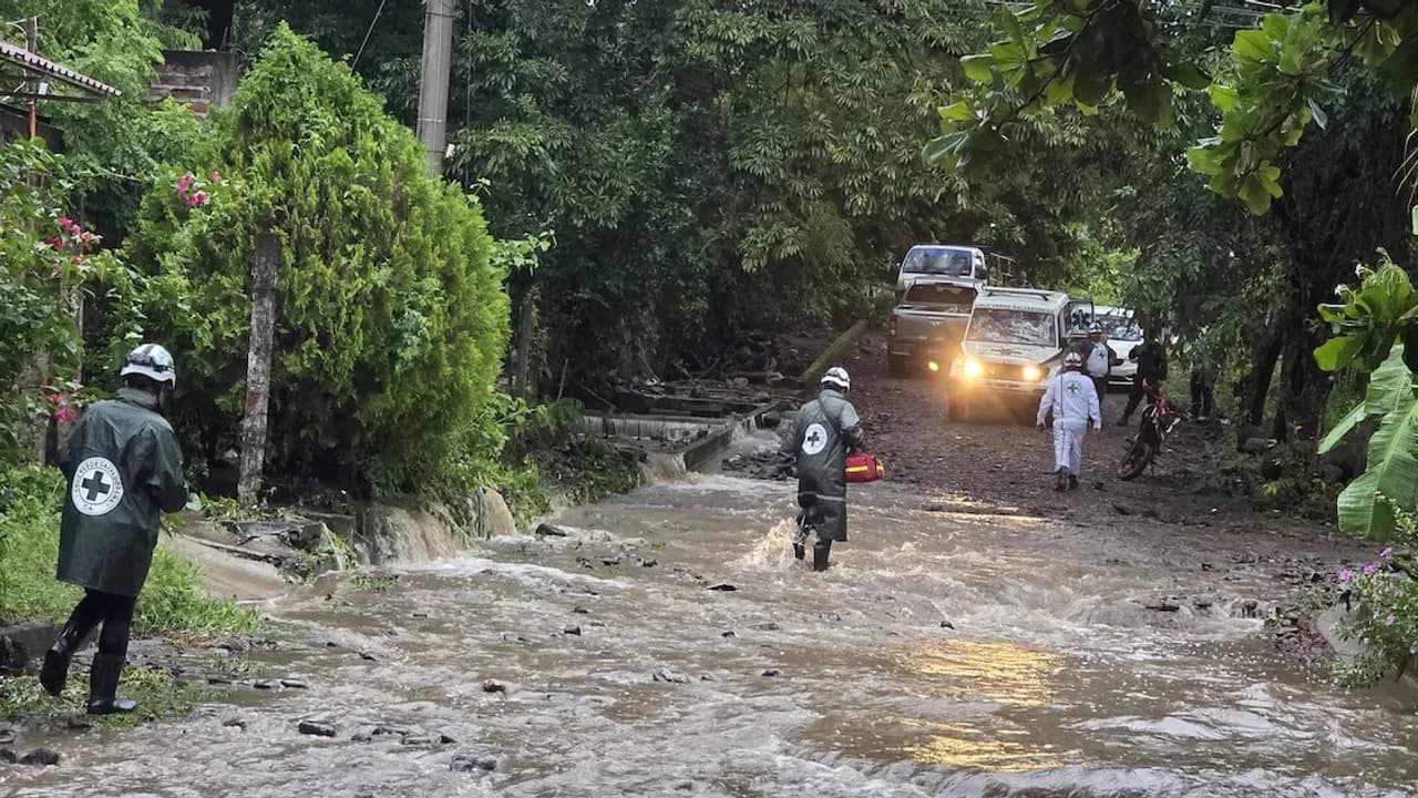 Socorristas de Cruz Verde caminan sobre una calle inundada con lodo y agua mientras un vehículo de auxilio aguarda.