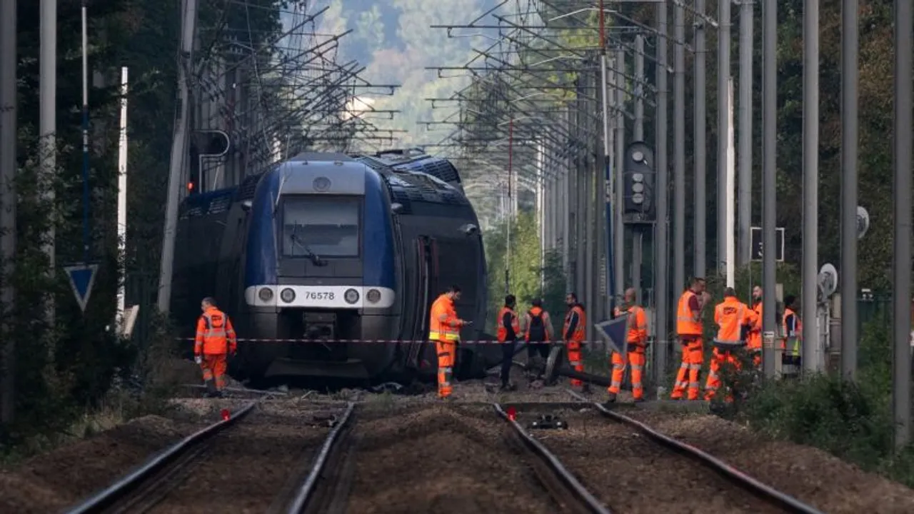 Un tren de pasajeros inclinado fuera de las vías rodeado por operarios con chalecos reflectantes naranjas.
