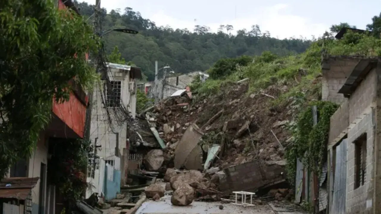 Derrumbe de tierra, piedras y escombros que cubre por completo una calle urbana entre viviendas en una ladera.