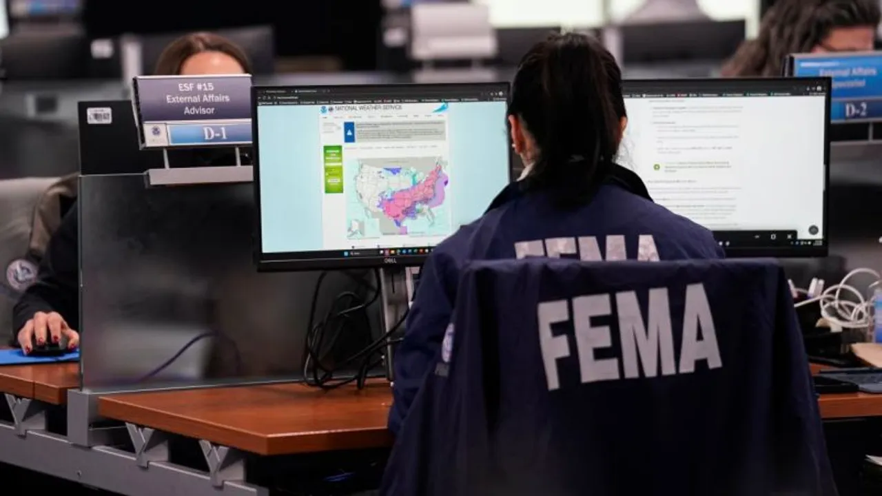 Una funcionaria de espaldas con campera de FEMA frente a computadoras de monitoreo de emergencias.