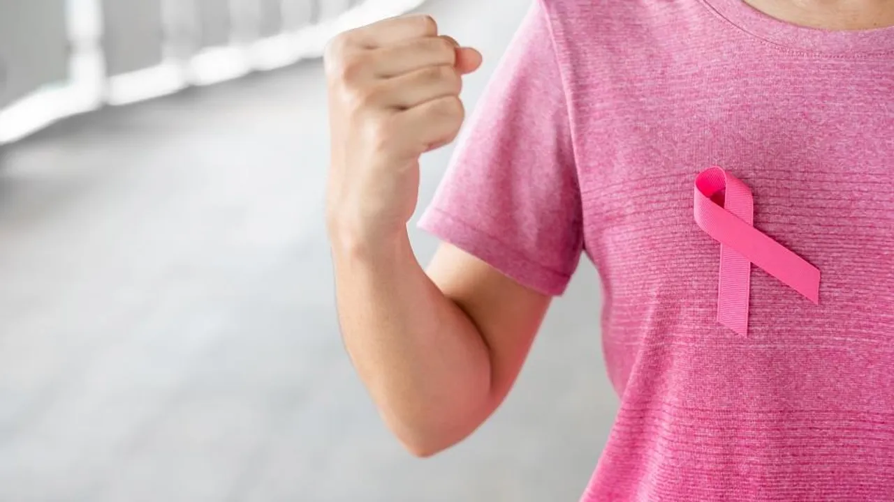 Persona con remera rosada y lazo rosa en el pecho que levanta el puño en señal de lucha y fortaleza.