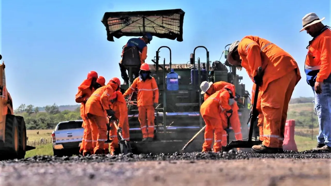 Obreros con uniformes de seguridad y cascos realizan labores de asfaltado en una ruta.