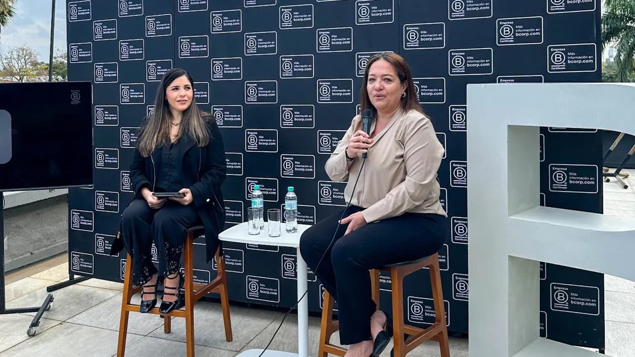 Dos mujeres sentadas en taburetes durante un panel frente a un fondo con logotipos de Empresa B Certificada.