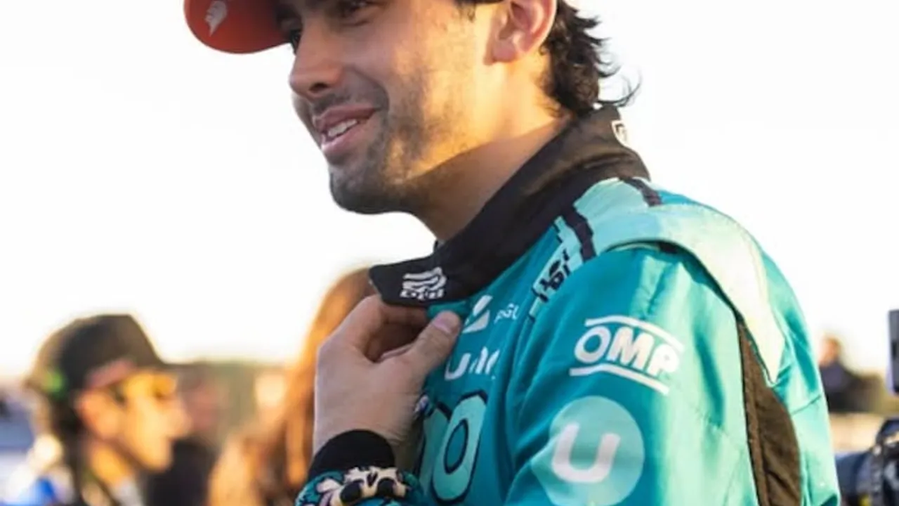 Piloto de carreras sonríe con buzo antiflama color turquesa y negro mientras ajusta el cuello de su indumentaria.