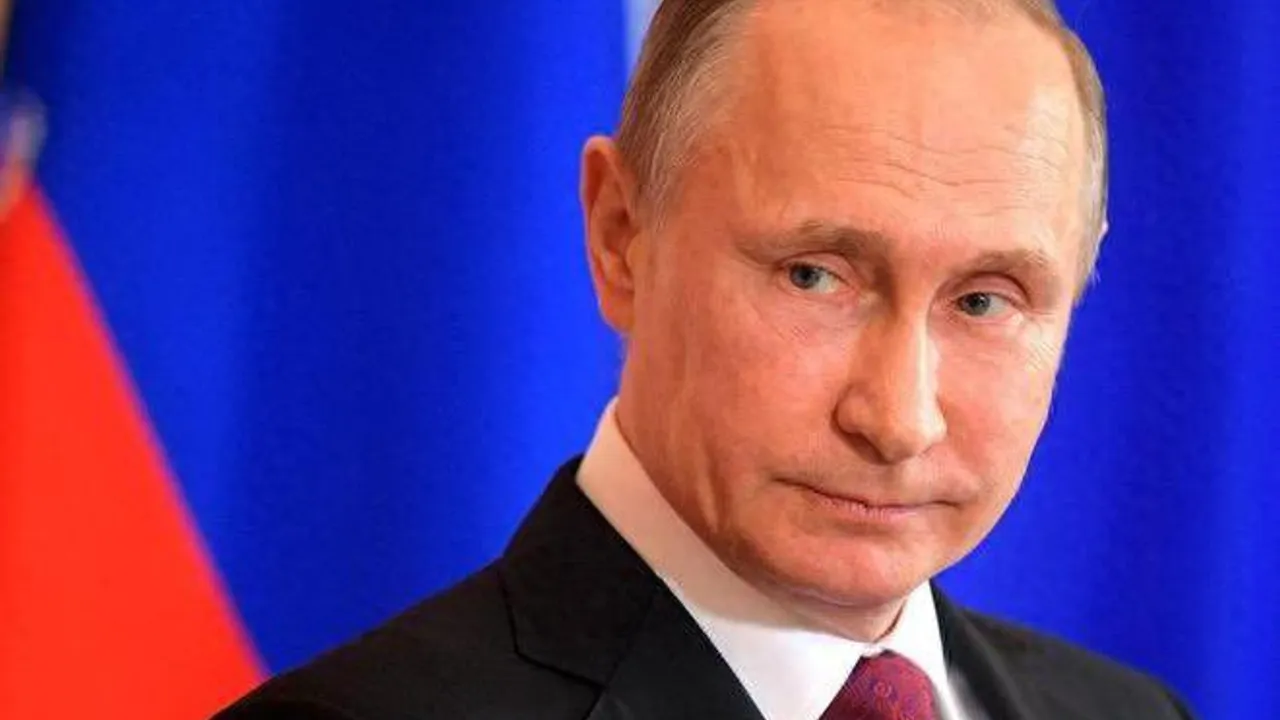 Vladimir Putin con traje oscuro y corbata bordó posa delante de una bandera azul y roja.