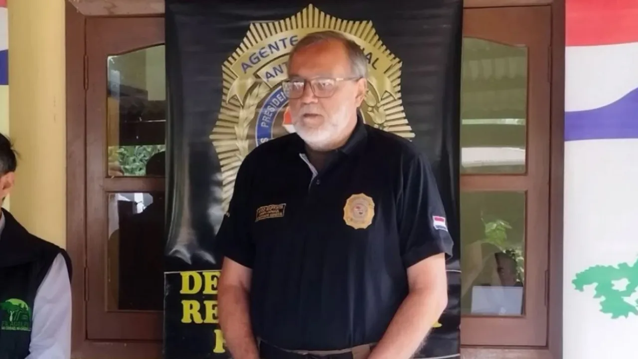 Hombre de barba y anteojos viste remera polo negra con insignia institucional en un acto oficial.